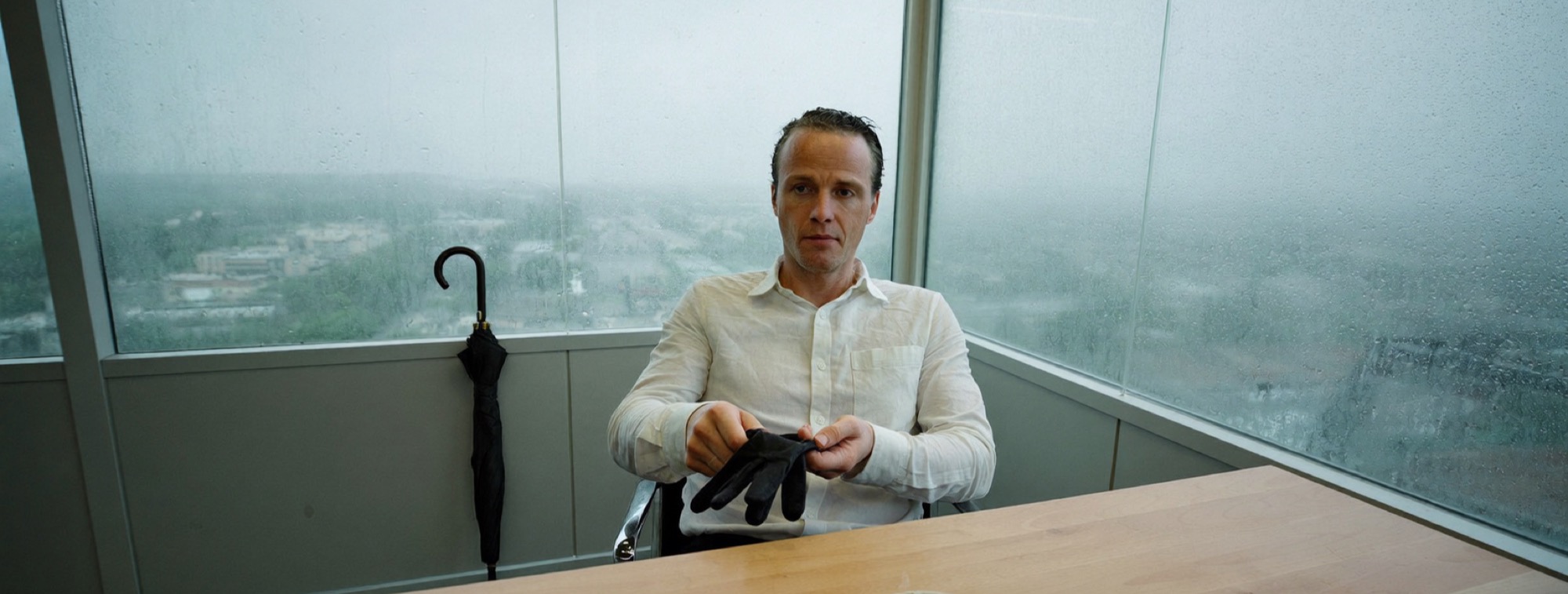 A founder at his desk on a rainy morning, pulling off a wet glove