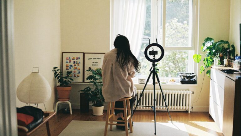 A creator seen from behind setting up a small camera and ring light in a bright living room