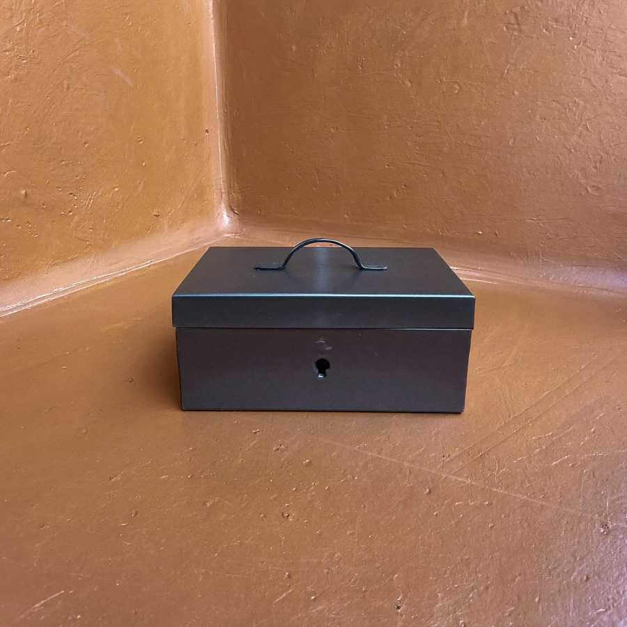 A small steel lockbox, closed, money put beyond easy reach on purpose
