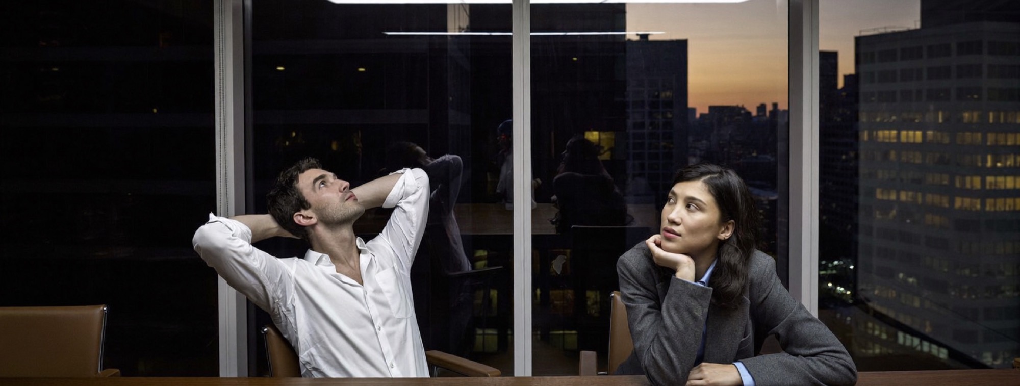 Two executives worn out at a boardroom table at the end of a long day