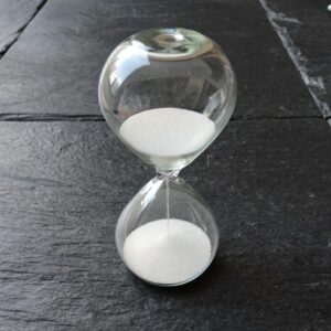 A glass hourglass of white sand on dark slate