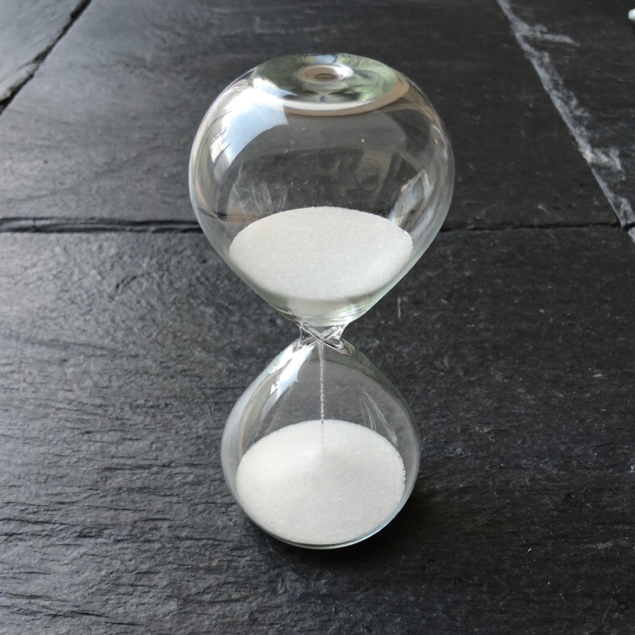 A glass hourglass of white sand on dark slate
