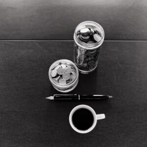 Two jars of coins of different heights, a fountain pen and an espresso cup