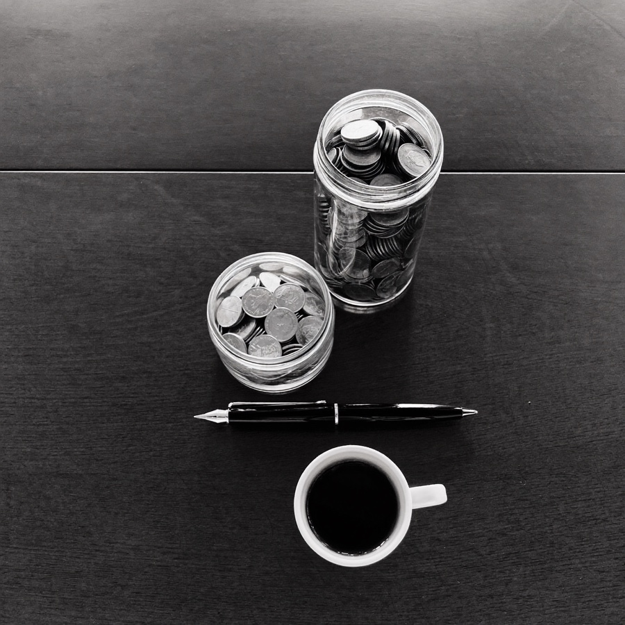 Two jars of coins of different heights, a fountain pen and an espresso cup