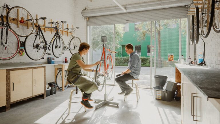 Hiring your first employee: a workshop owner training a new hire on a bicycle wheel
