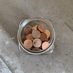 A glass jar full of copper coins on polished concrete