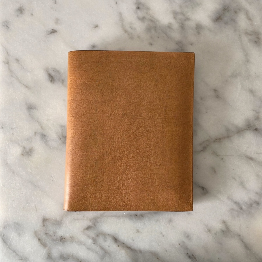 A closed tan leather wallet on white marble