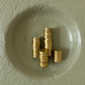 Three uneven stacks of gold coins on grey-green plaster