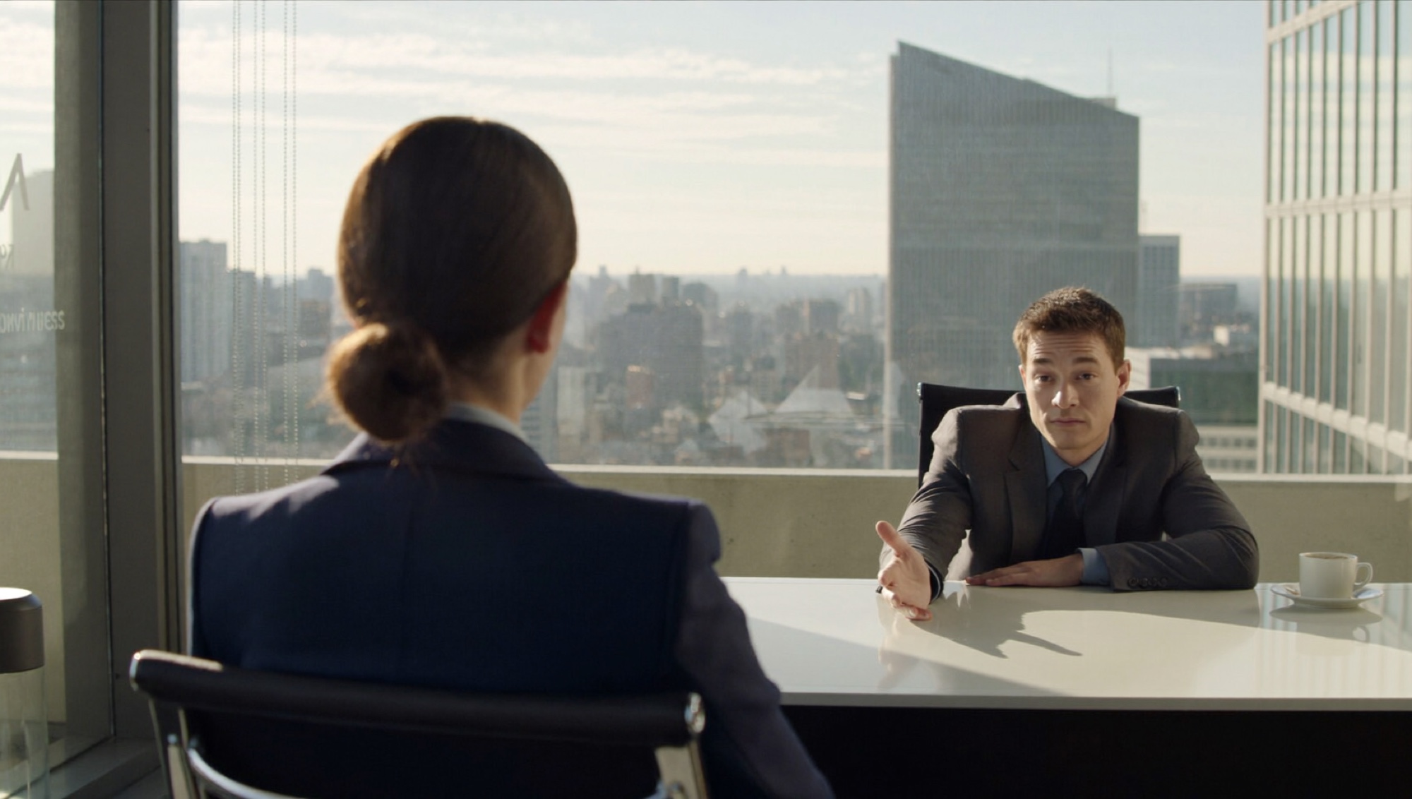 A colleague leans across a manager's desk to ask for something