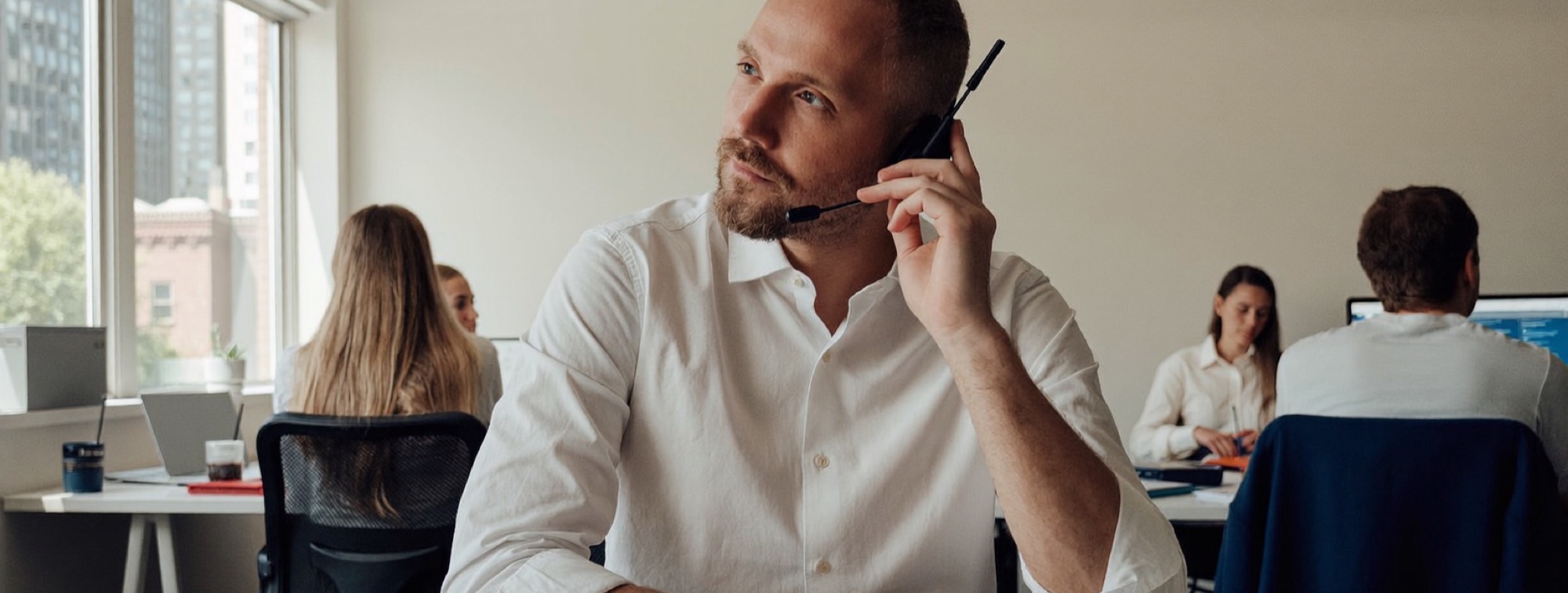 A founder listening on a headset call at his desk in an open-plan office