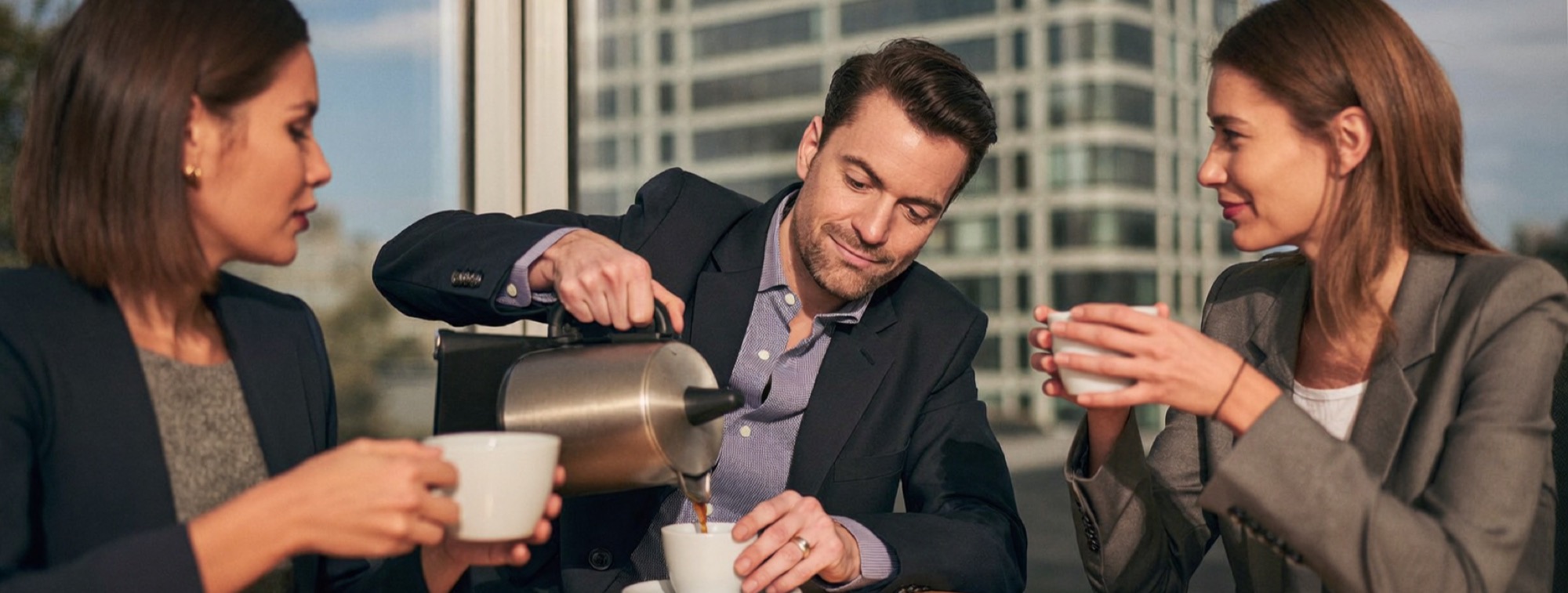 A small-business owner and her accountant share a coffee at the corner of a meeting table