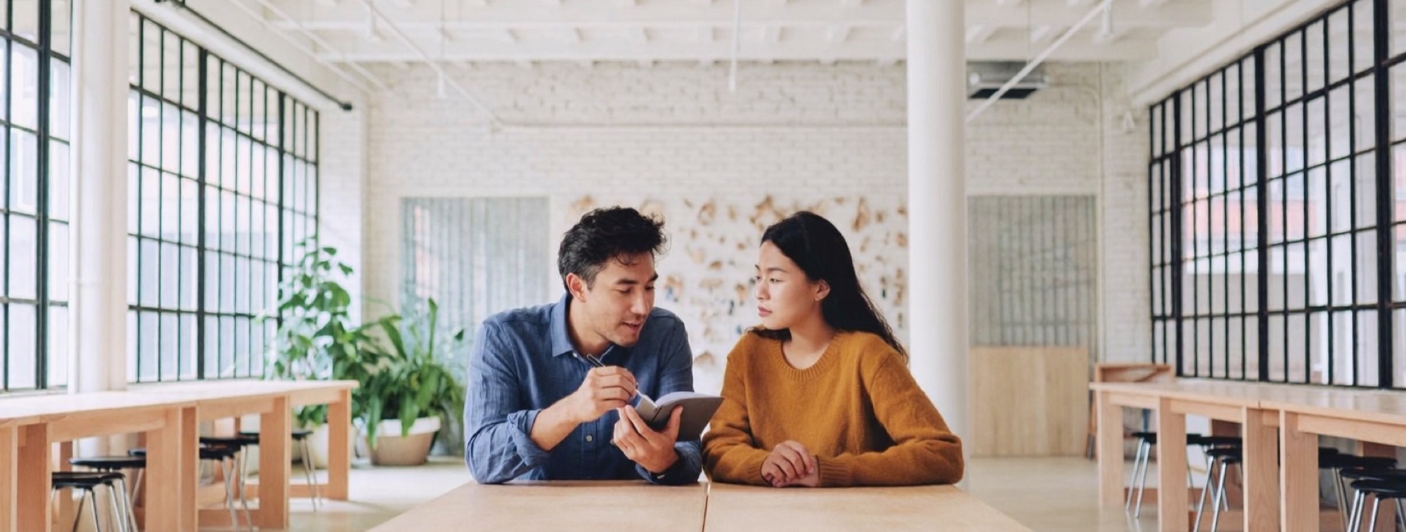 Two founders in a co-working loft, one reading a line aloud while the other listens for the tell