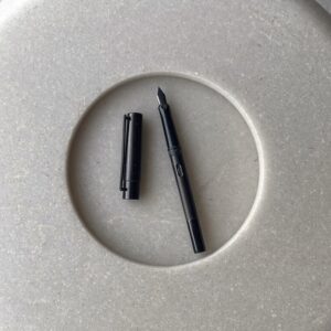 An uncapped black fountain pen on pale grey stone