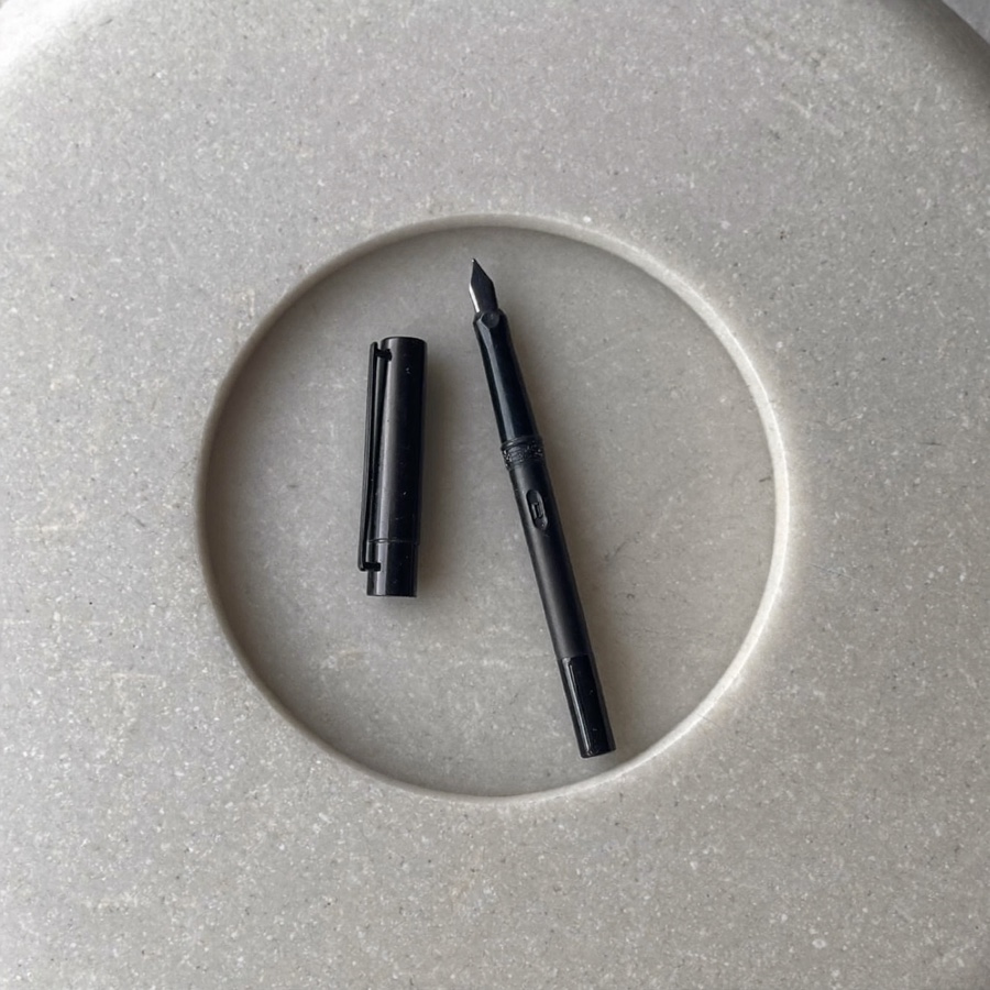 An uncapped black fountain pen on pale grey stone
