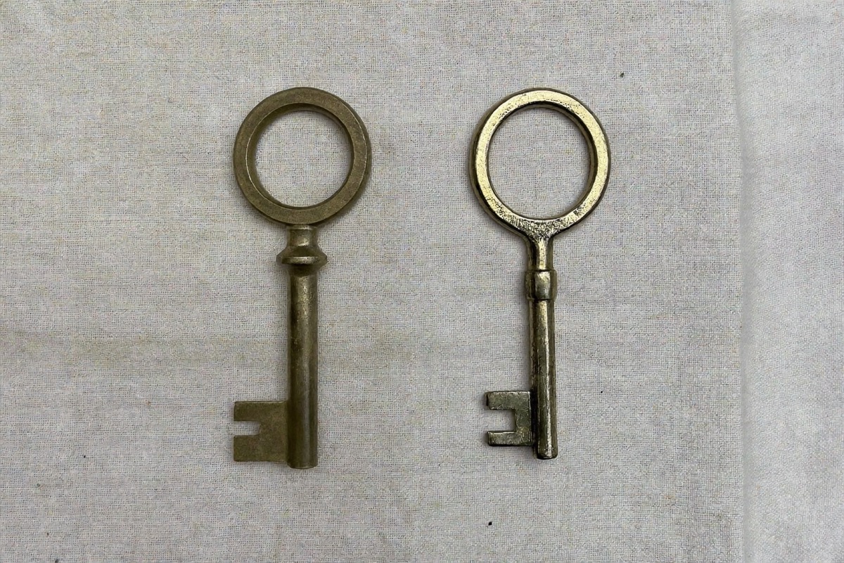 Two nearly identical brass keys with different teeth, one word separating two compensation models