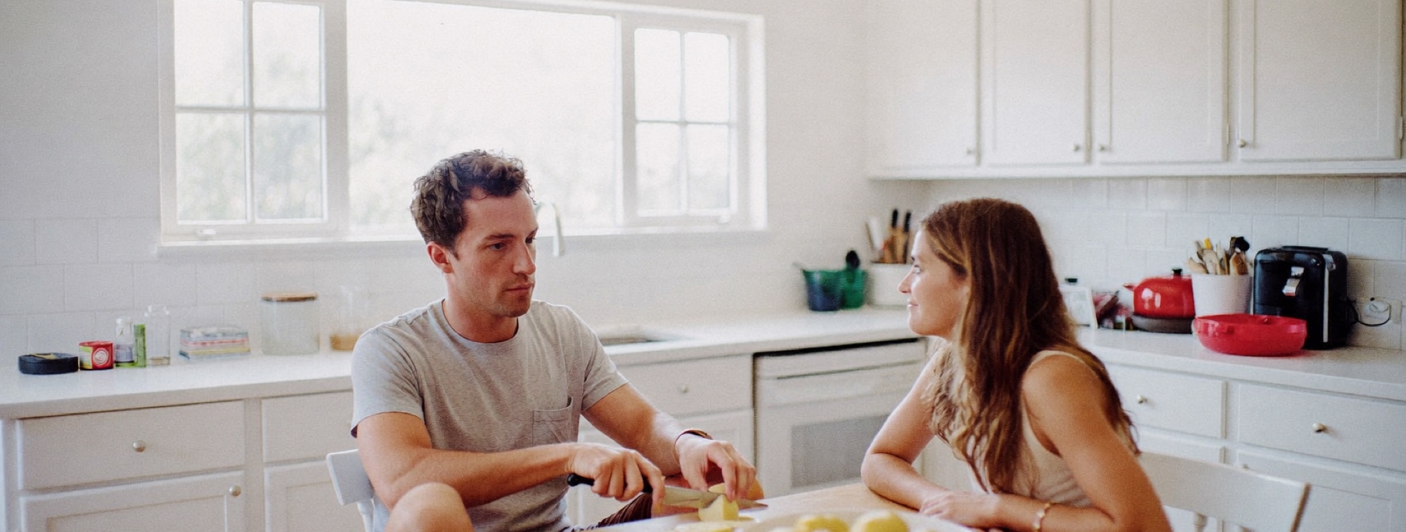 Two people talking over breakfast in a bright kitchen on a Saturday morning
