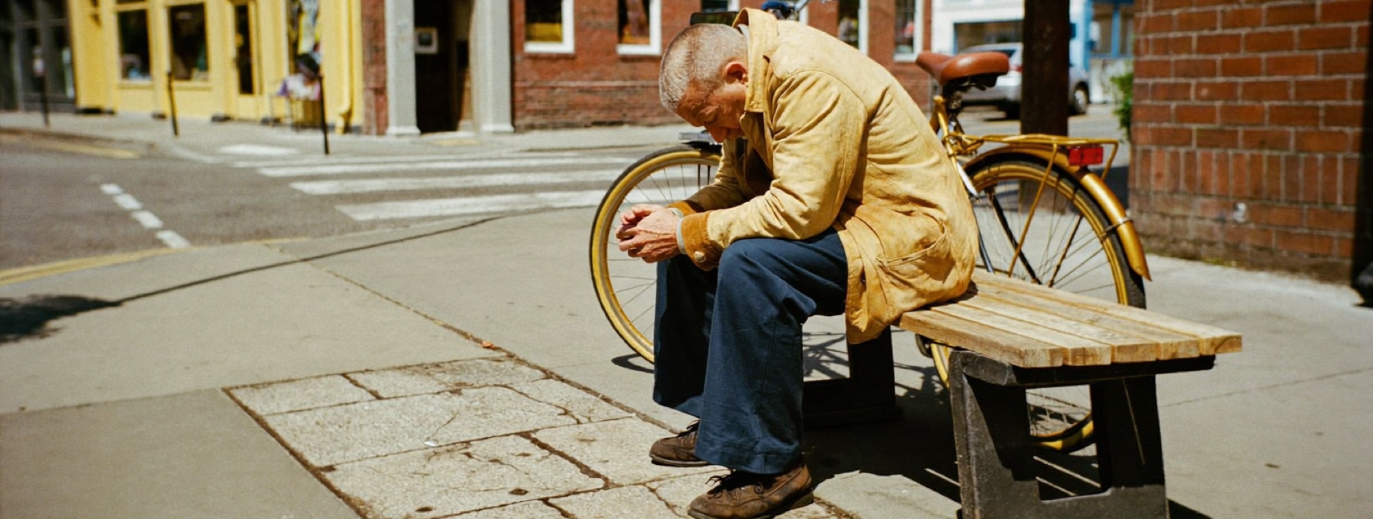 A man on a bench outside a small-town bank, deciding what kind of help his money needs