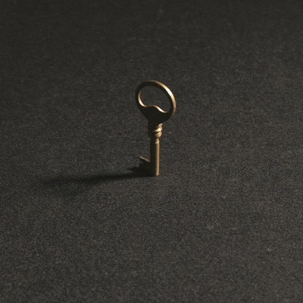A single brass key upright on a dark charcoal surface, the one word that unlocks how an advisor is paid