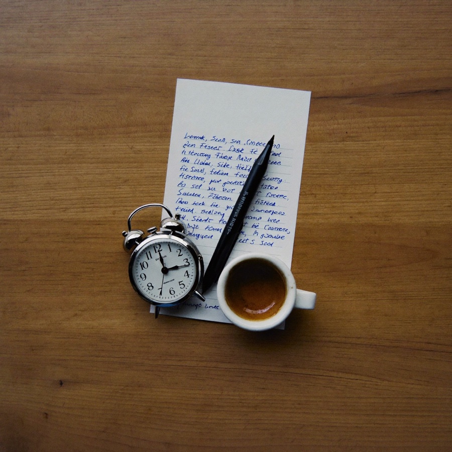 An overhead cluster of a small clock, a pen and an empty espresso cup