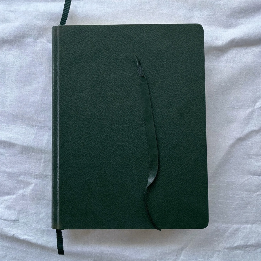 A closed green leather notebook with its ribbon marker left halfway through