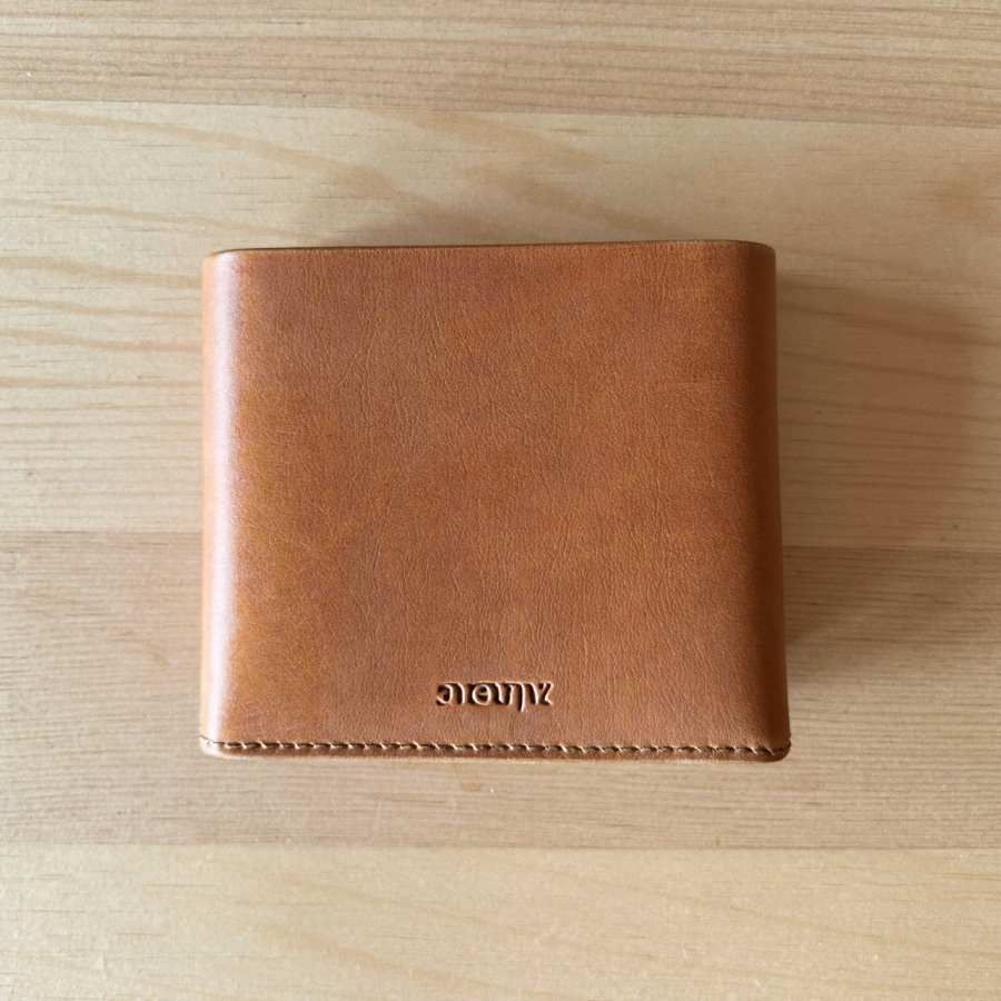 A closed tan leather wallet on pale oak