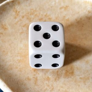 A single white die on pale stone