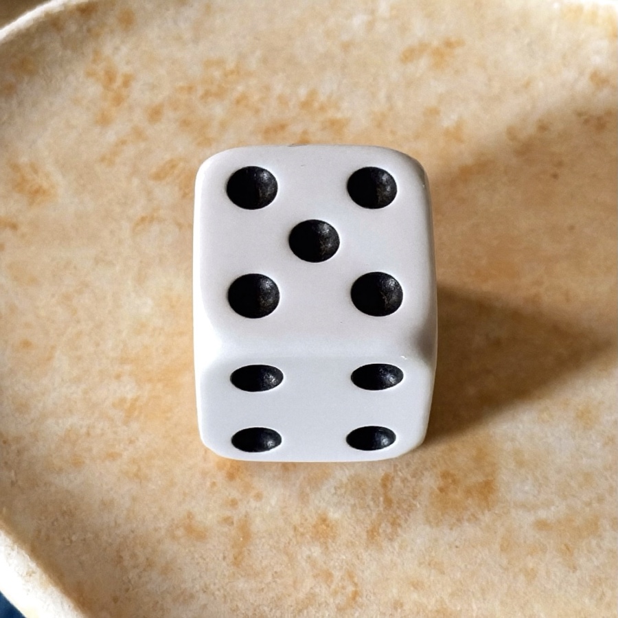 A single white die on pale stone