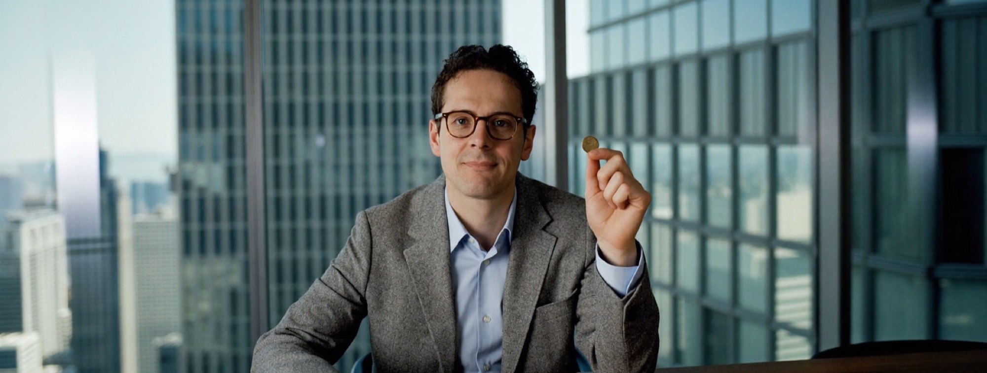 A man at a meeting table holding up a single coin