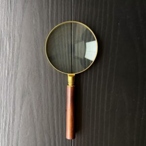 A brass magnifying glass on matt black painted wood