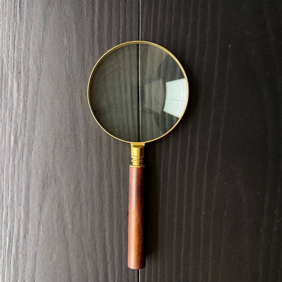 A brass magnifying glass on matt black painted wood