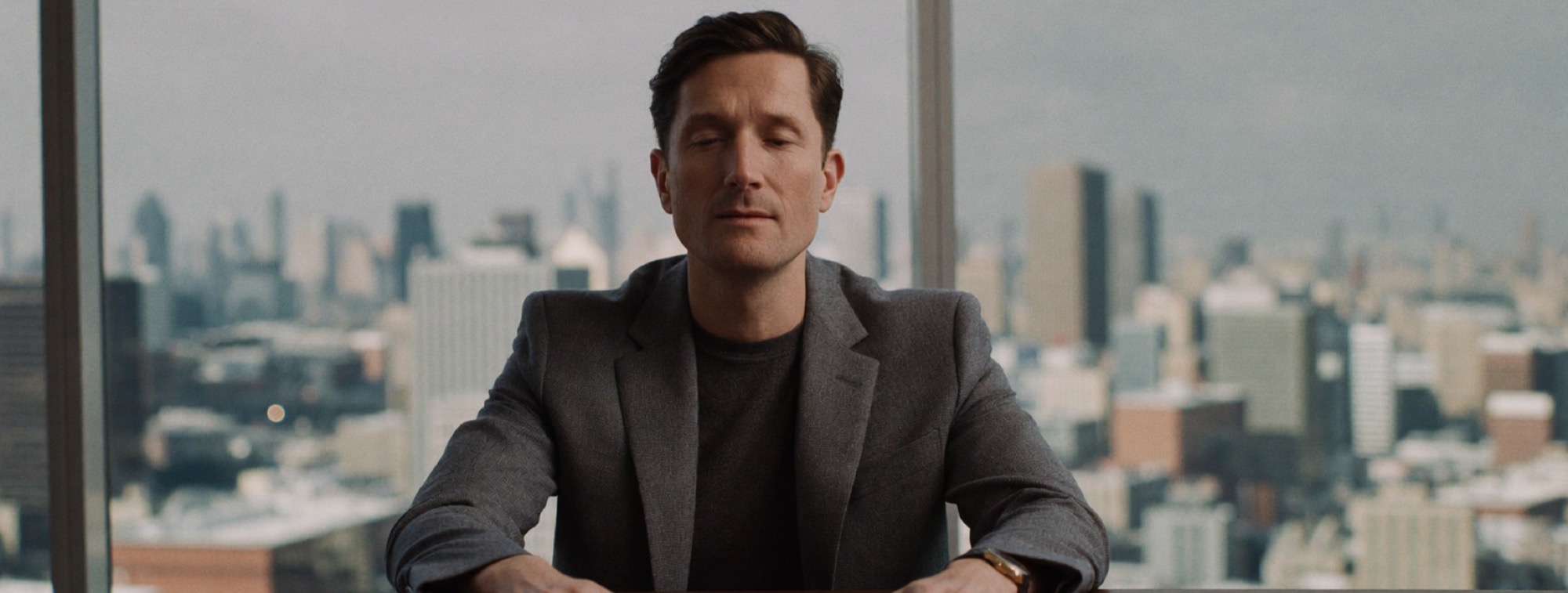 A man at a meeting table, palms flat, eyes closed, very still