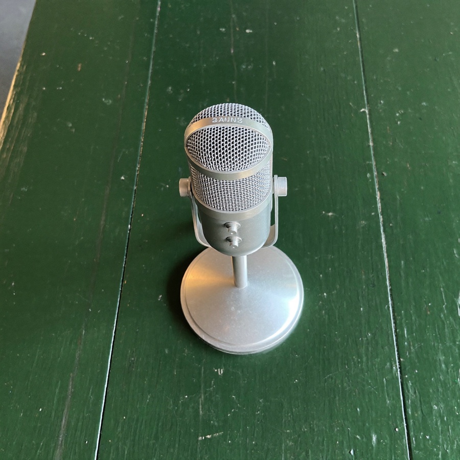 A silver broadcast microphone on deep green painted wood