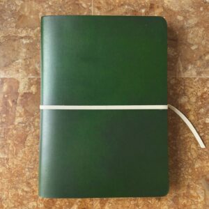 A closed green leather notebook held shut by a cream band, on warm stone