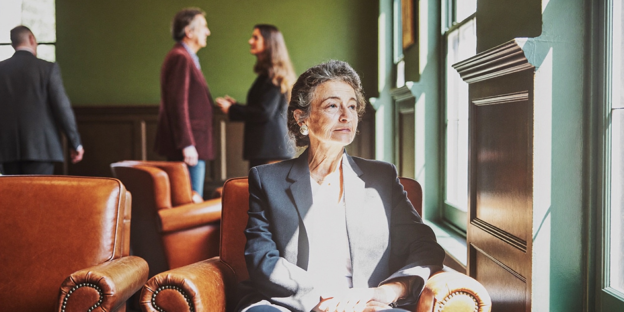A director seated by a tall window in the early light before her first meeting of the day
