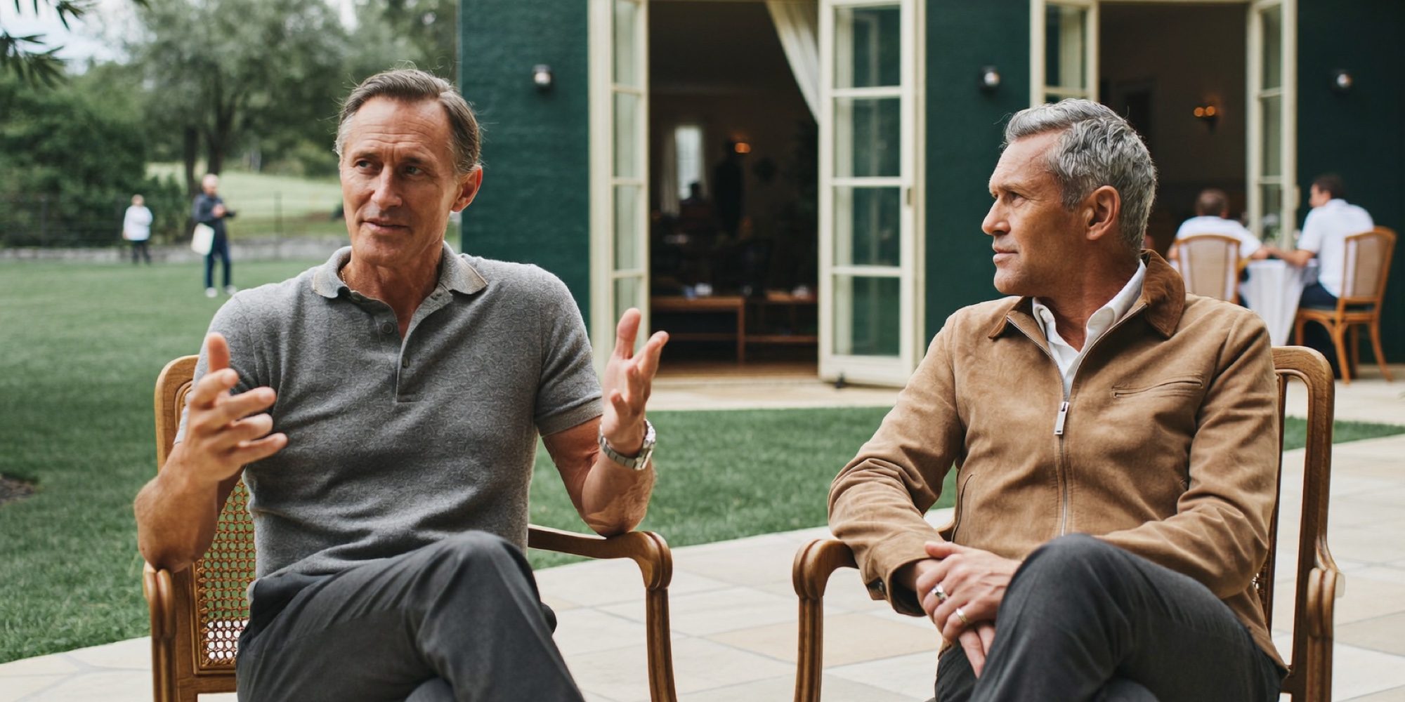 Two executives at an offsite in knitwear and a suede jacket, both reading the dress code correctly