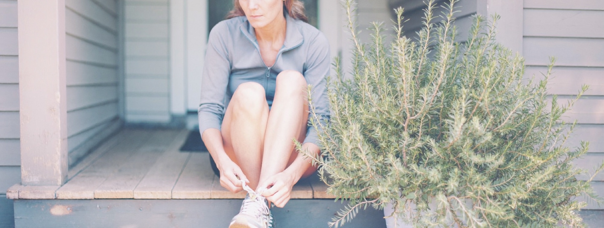 A woman lacing her running shoes in morning sun, using daylight to set her body clock