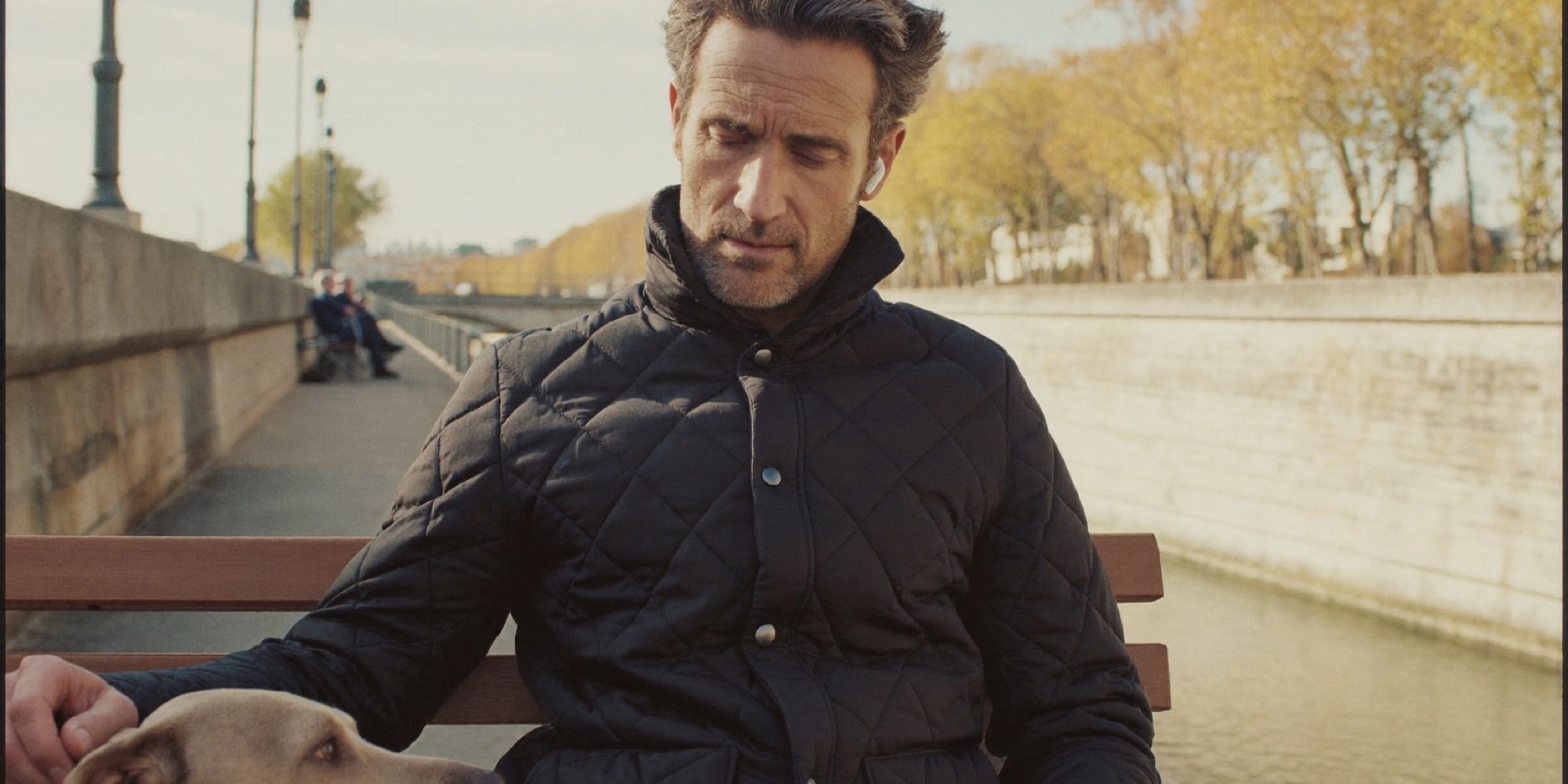 A man listening to a podcast on a park bench by the river