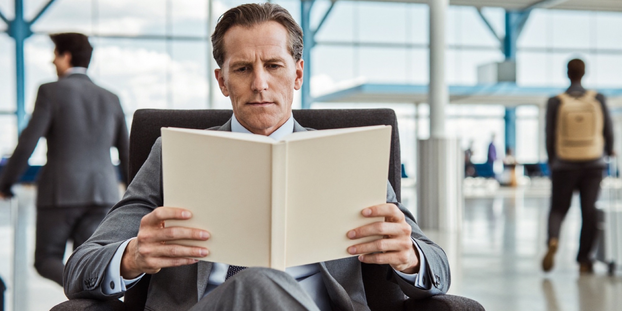 A director with a book on his knee in an airport lounge, thinking over a chapter before his flight